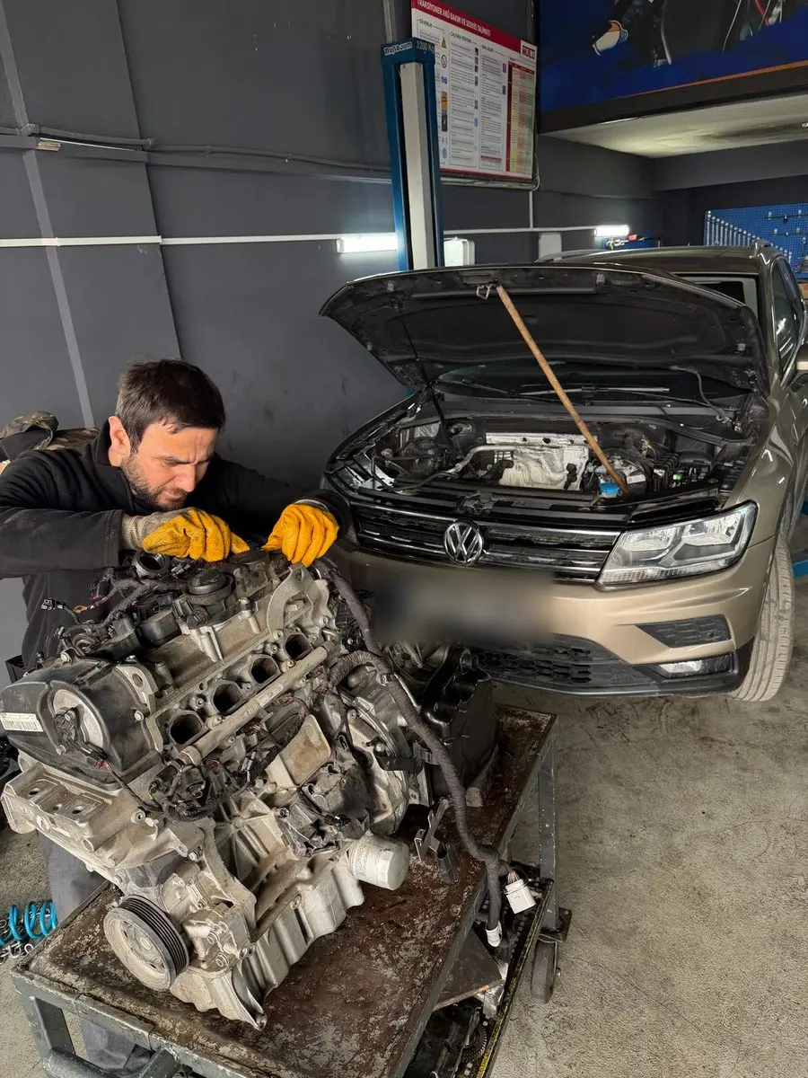 Sökülen motor üzerinde çalışan teknisyen, arkada kaputu açık Volkswagen Tiguan